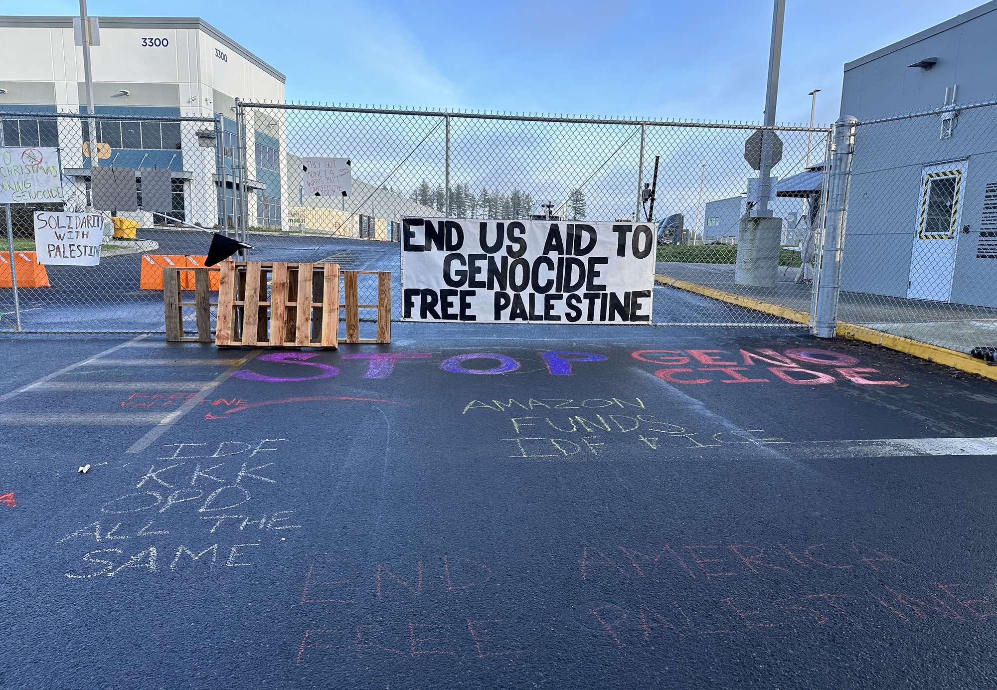 Uno striscione attaccato a una cancellata di un magazzino Amazon che dice: «End US Aid to genocide. Free Palestine»