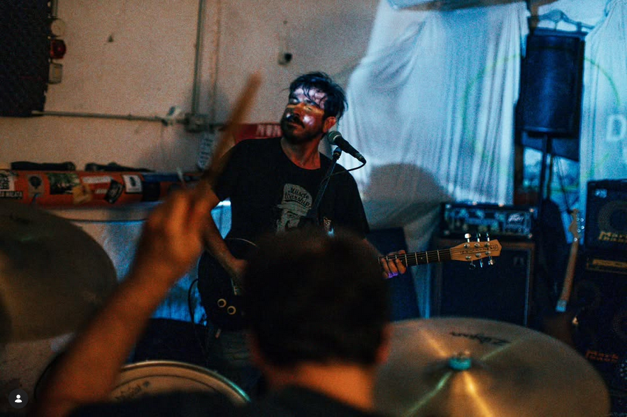 Sul fondo, con un muro alle spalle e di fronte a noi, c'è un tizio che sta suonando una chitarra. Sulla destra si notano degli amplificatori e un'altra chitarra sul suo piedistallo. Il corpo della chitarra e quello del chitarrista sono parzialmente coperti dal batterista, che vediamo di spalle in sovrimpressione, la testa bassa e il braccio sinistro alzato nell'atto di colpire la batteria, della quale si vedono due piatti e un tom