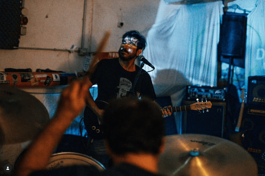 Sul fondo, con un muro alle spalle e di fronte a noi, c'è un tizio che sta suonando una chitarra. Sulla destra si notano degli amplificatori e un'altra chitarra sul suo piedistallo. Il corpo della chitarra e quello del chitarrista sono parzialmente coperti dal batterista, che vediamo di spalle in sovrimpressione, la testa bassa e il braccio sinistro alzato nell'atto di colpire la batteria, della quale si vedono due piatti e un tom